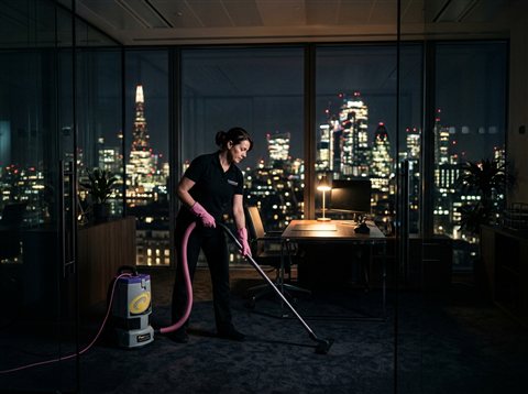 Cleaner vacuuming an empty office at night with city lights outside